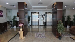A modern lobby with a marble floor, two elevators, potted plants, and a reception desk with a vase of flowers. - Magic Suite Mahboula-5 (Mahboula)