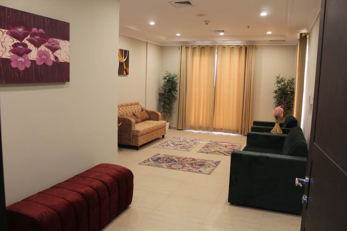 A living room with a sofa, a bench, and a coffee table. There are two potted plants and a painting on the wall.