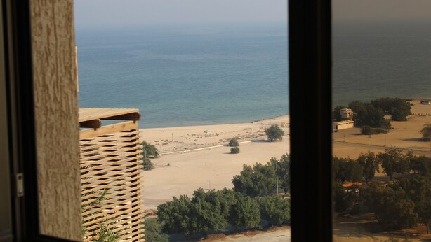 A view of a beach from a window, including a wooden structure and a sandy area with trees. - Magic Suite Mahboula-5 (Mahboula)