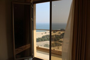 A room with a large window overlooking a beach and a forested area. - Magic Suite Mahboula-5 (Mahboula)