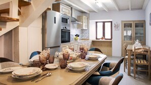 A dining area with a long table set for a meal, a kitchen with modern appliances, and a staircase leading to another level. - Country house in Llanes for trips with family or friends  (Soberron, Llanes)