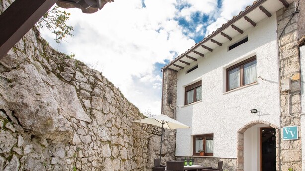 A stone building with a white exterior, a balcony with wicker furniture, and a potted plant. - Country house in Llanes for trips with family or friends  (Soberron, Llanes)