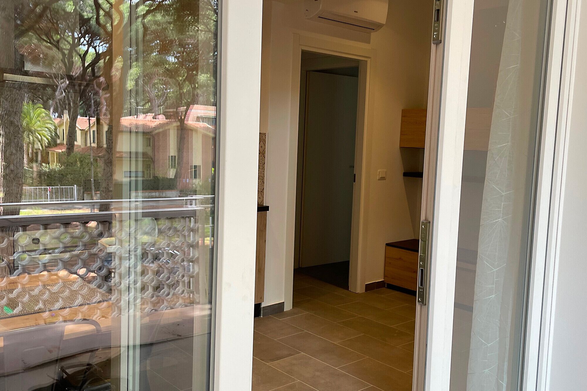 Ein Hotelzimmer mit Glastür zu einem Balkon, gefliestem Boden und sichtbarer Klimaanlage.