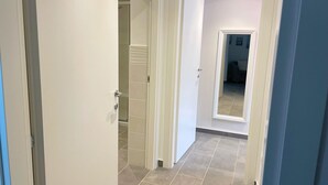 Ein Flur mit einer weißen Tür, die zu einem Badezimmer mit Dusche und Fliesenboden führt.