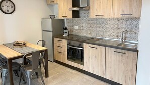 Eine kleine Küche mit Holzausstattung, einem Edelstahlkühlschrank, einem eingebauten Backofen und einem Spülbecken.