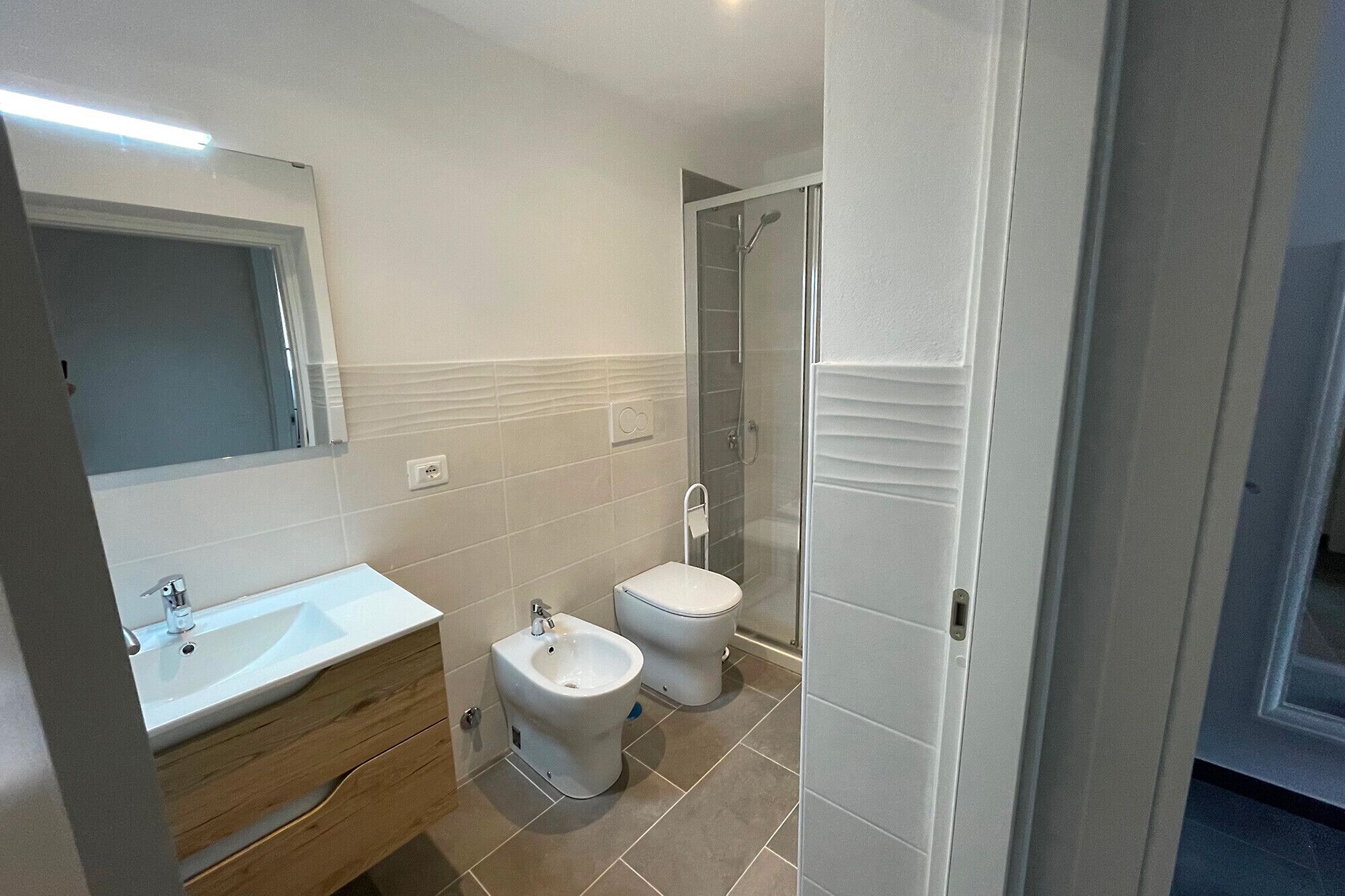 A modern bathroom with a sink, bidet, toilet, and a glass-enclosed shower.