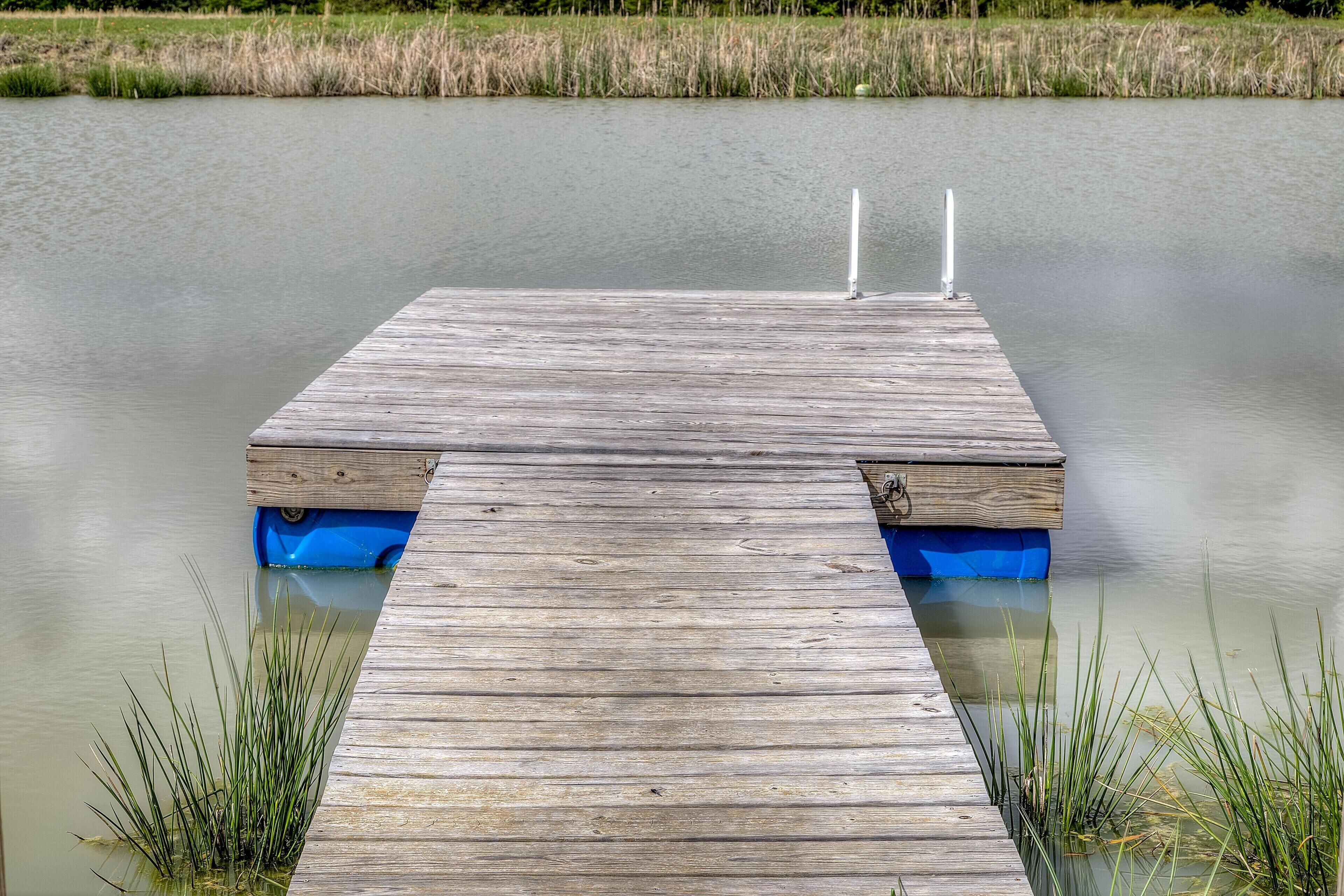 A wooden dock extending into a calm body of water with grassy banks.
