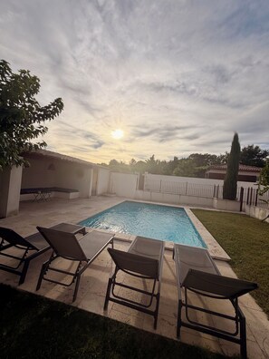 A rectangular swimming pool with a tiled deck, surrounded by a low fence, and equipped with several lounge chairs.