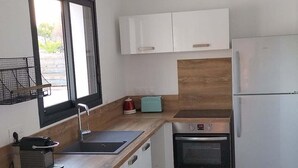 Une cuisine compacte avec des meubles blancs, un four encastré, un réfrigérateur, une fenêtre offrant une belle vue et des carreaux de sol à motifs.