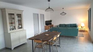 Un coin repas avec une table et des chaises en bois, un buffet blanc aux portes vitrées et, au fond, un canapé de couleur turquoise.