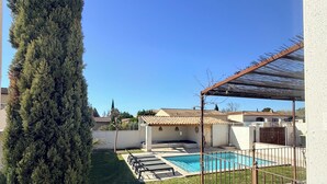 Un jardin avec une piscine, un grand arbre à feuilles persistantes et une pergola.