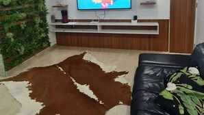 Una sala de estar con un televisor montado, un sofá de cuero, un tapete de cuero de vaca y una pared verde con plantas.