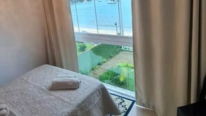 Un dormitorio con un ventanal grande, una cama y vistas a una masa de agua y vegetación.