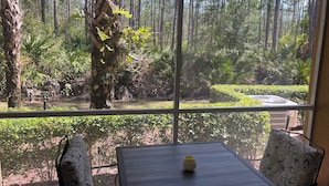 Une pièce dotée d’une grande fenêtre donnant sur une zone boisée. On y trouve une table sur laquelle est posé un seul objet décoratif.