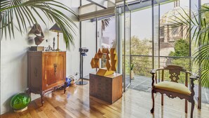 A spacious room with a wooden floor, a large window offering a view of greenery and buildings, a wooden cabinet, a chair, and a lamp. - Amazing PH w/great terrace in the heart of Condesa (Mexico)