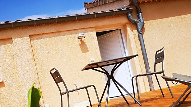 An outdoor patio with a table and two chairs, a tiled roof, and a beige wall. - 1 Bedroom Apartment in Aubenas (Aubenas)
