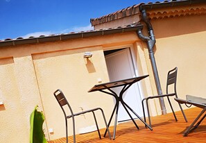 Un patio exterior con una mesa y dos sillas, un techo de baldosas y una pared color beige.