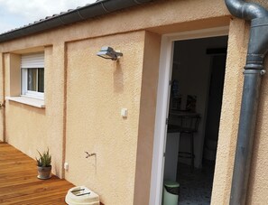 Exterior de un edificio con una terraza de madera, una ventana, una luz fijada a la pared y una puerta de entrada.