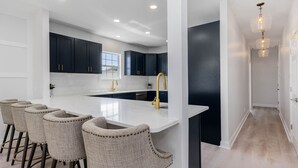 Une cuisine moderne dotée d’un grand îlot central, de meubles de couleur sombre et d’un plan de travail blanc.