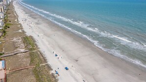 Une plage avec une longue étendue de sable, quelques parasols et quelques personnes.