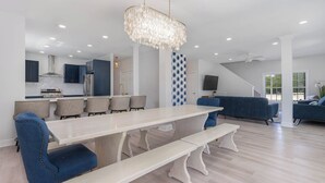 Une cuisine moderne avec des meubles blancs, une grande table à manger et des chaises recouvertes d’un tissu bleu.