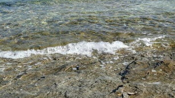 Une vue dégagée sur la côte, avec un rivage rocheux, une mer calme et un bateau au loin.