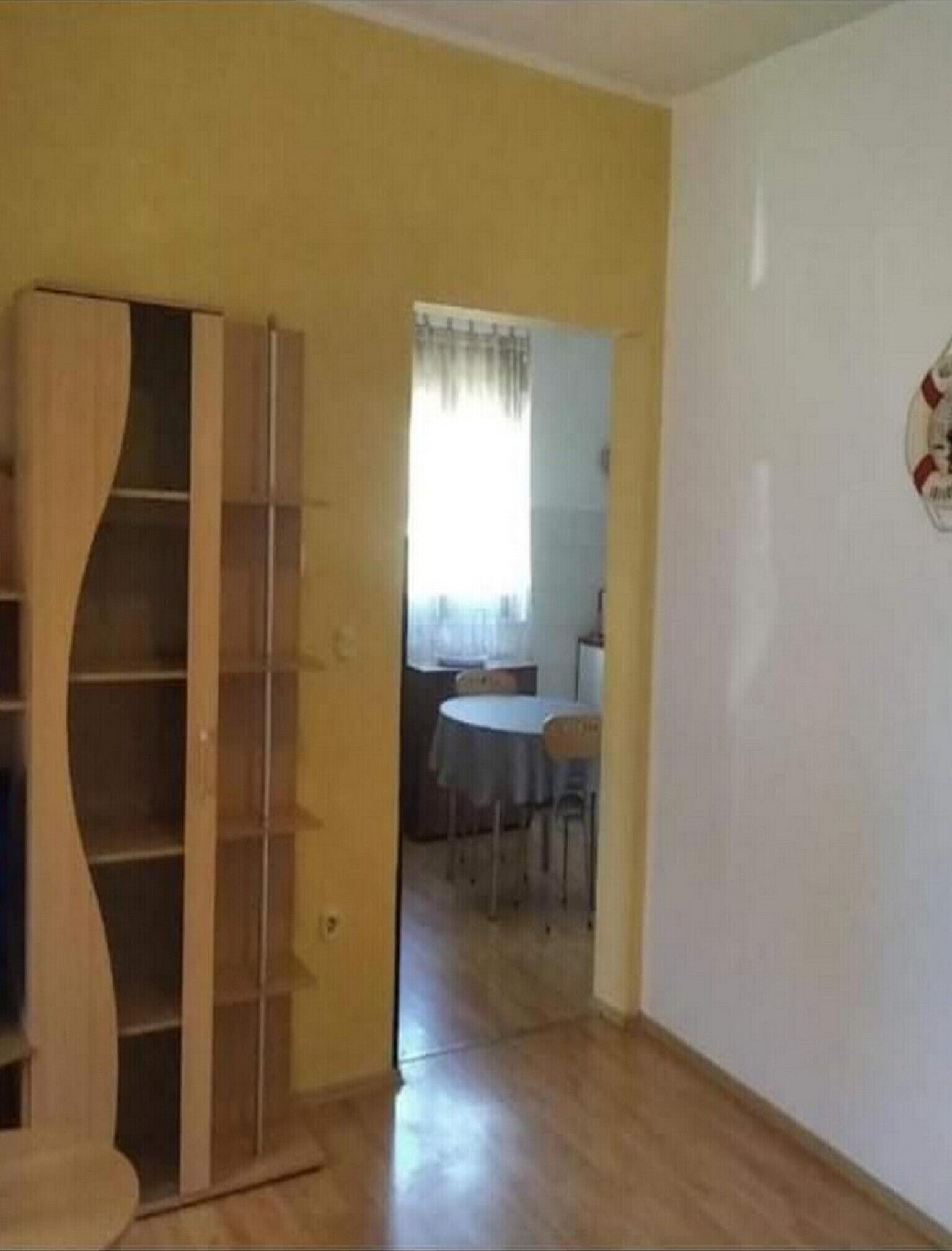 Ein Zimmer mit einem Holzschrank, einem Esstisch mit Stühlen und einer weißen Wand mit einem kreisförmigen Wappen.