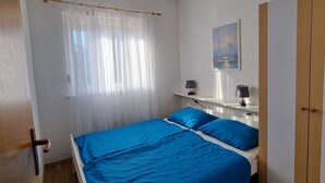 A bedroom with a bed, a bedside table with a lamp, a wardrobe, and a window with curtains.