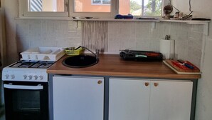 A compact kitchen with a gas stove, oven, and a small refrigerator. There are two windows above the sink, and a microwave is mounted on the wall.