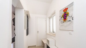 Un pasillo estrecho con una puerta blanca, un banco y una ventana.