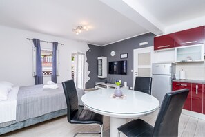 Une chambre d’hôtel moderne comprenant un lit, une table de salle à manger ronde avec des chaises, un téléviseur et une kitchenette avec des placards rouges.