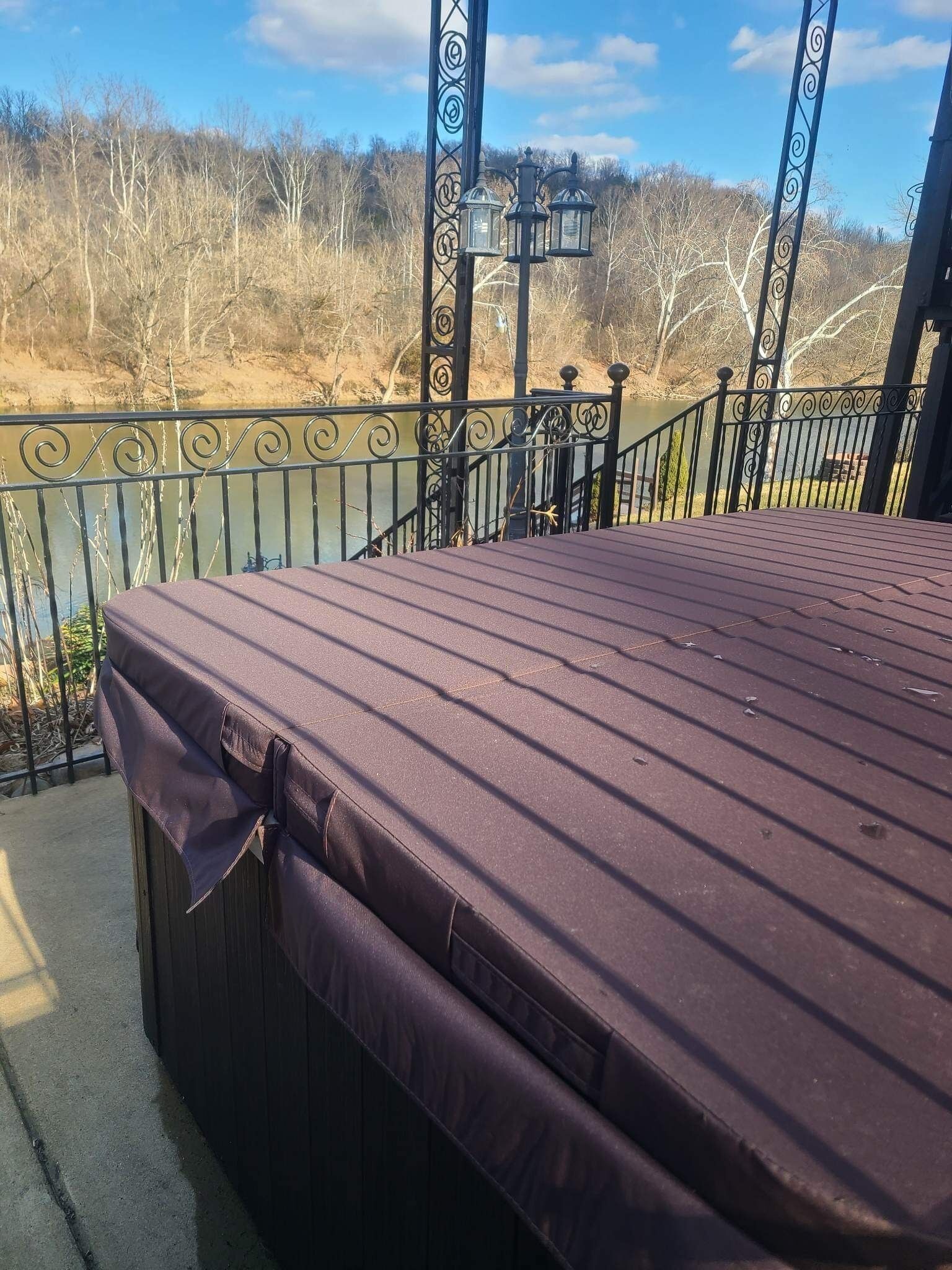 A covered outdoor area with a metal railing and a view of a body of water and trees.