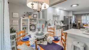 Une cuisine moderne avec des meubles blancs, un îlot central et un coin repas agrémenté de chaises en bois et d’une nappe bleue.