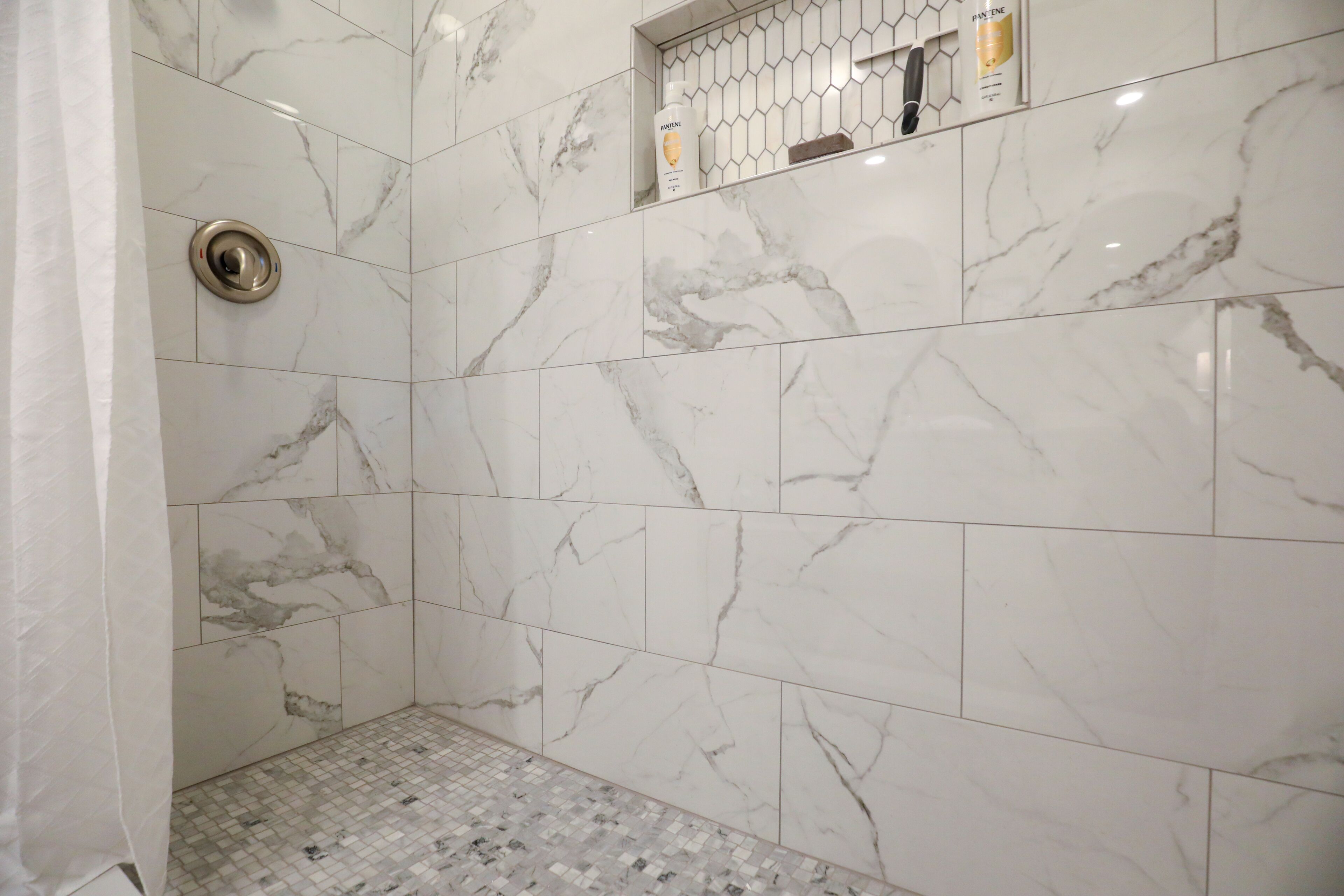A bathroom with white marble tiles and a shower area.