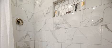 A bathroom with white marble tiles and a shower area.
