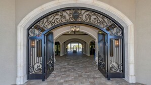 Une entrée en arc surmontée d’une ferronnerie ouvragée, qui mène à un couloir carrelé illuminé par un lustre.