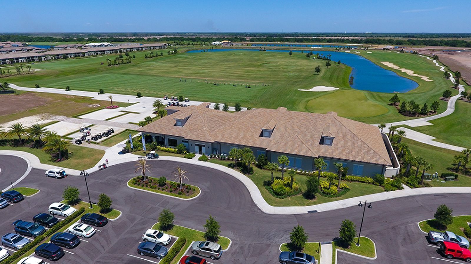 Vue aérienne d’un terrain de golf avec un club-house, un parking et la végétation environnante.