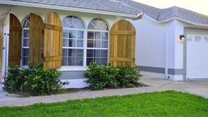 A residential house with a garage, a covered porch with wooden shutters, and a well-maintained lawn. - 594 Sandy Shore Château w Heated Pool | Walk2Beach (Naples)