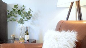 A room with a brown leather sofa, a white fluffy pillow, a vase with green leaves, a bottle of wine, and a lamp. - 594 Sandy Shore Château w Heated Pool | Walk2Beach (Naples)