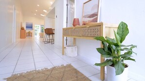 A hallway with a white tiled floor, a wooden console table with storage, a potted plant, and a framed picture on the wall. - 594 Sandy Shore Château w Heated Pool | Walk2Beach (Naples)