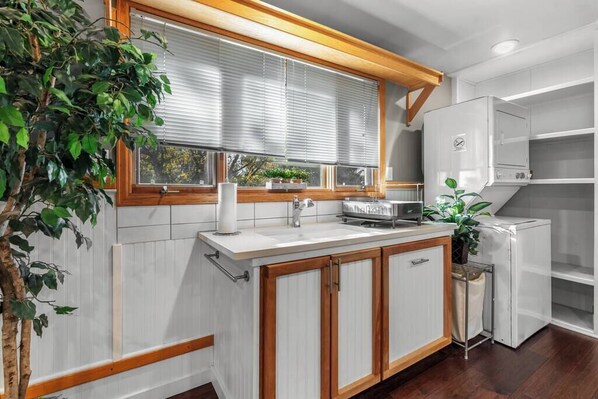 A kitchen with white cabinets, a wooden countertop, a sink, a stove, and a window with blinds.