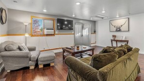 Un salon moderne avec un canapé gris, un canapé vert, une table basse en bois et un téléviseur fixé au mur.