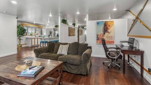 Un salon moderne avec un canapé, une table basse et un coin repas. Il y a une affiche accrochée au mur et un bureau d’ordinateur.