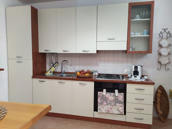 Una cucina con mobili bianchi, un lavandino in acciaio inox, un fornello e una macchina per il caffè.