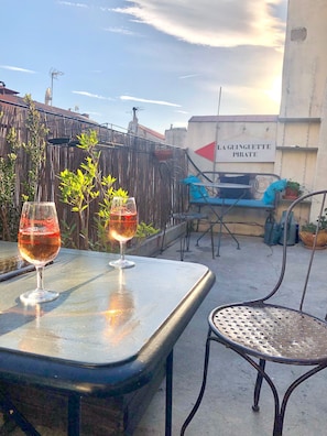 Una terraza en la azotea con dos copas de vino sobre una mesa, una silla y un letrero que dice "LA GUINGUETTE PIRATE".