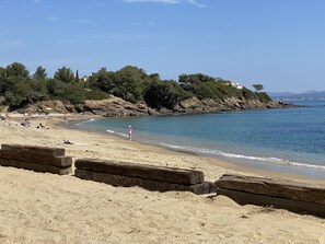 A beach with clear blue water, sandy shore, and rocky cliffs with trees.