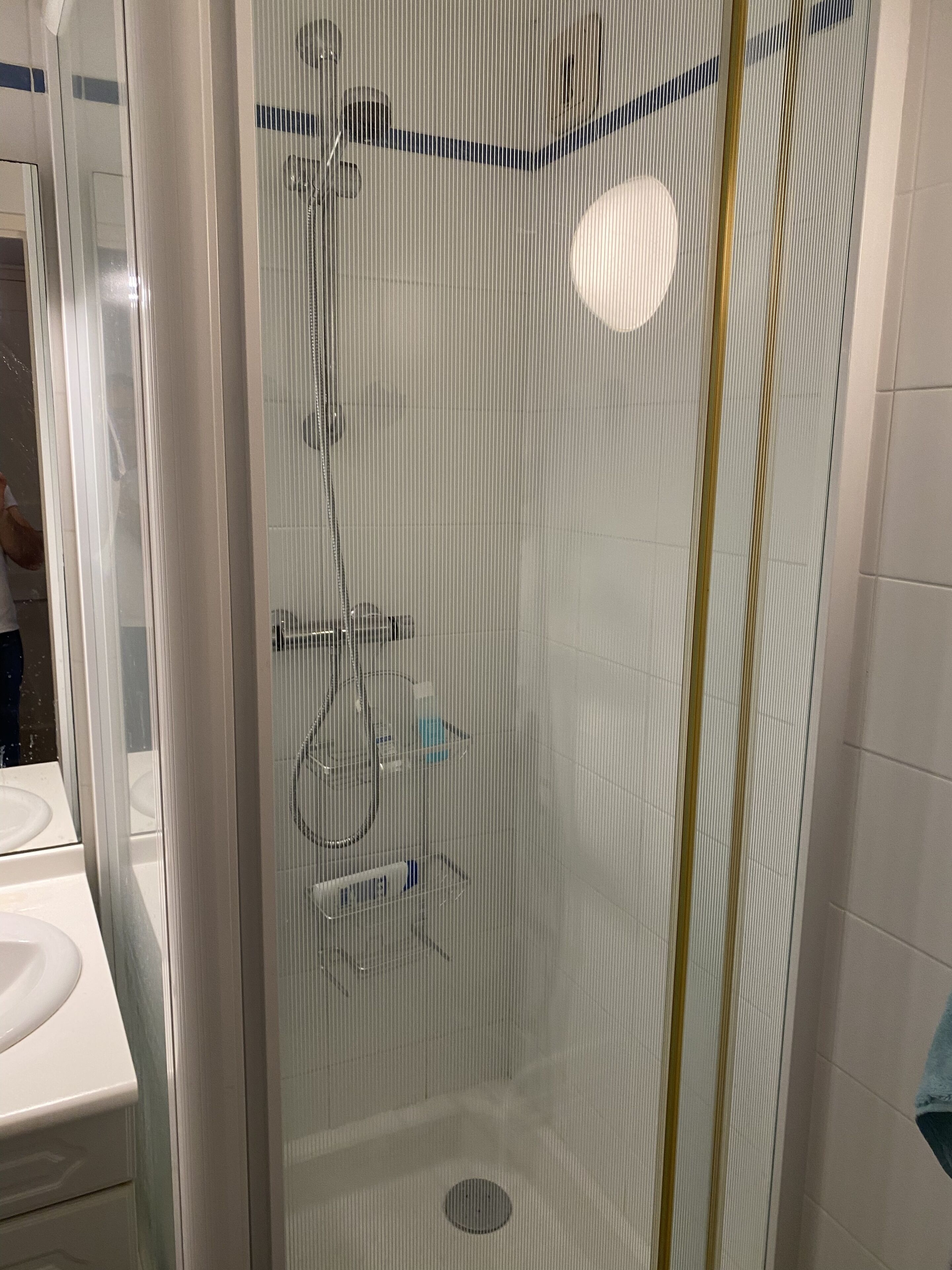 A shower enclosure with a glass door, a handheld showerhead, a wall-mounted faucet, and a small shelf with toiletries.