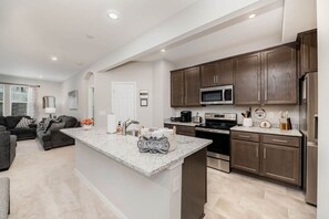 A modern kitchen with dark wood cabinets, a granite countertop, stainless steel appliances, and a built-in island with a 'Welcome' sign.