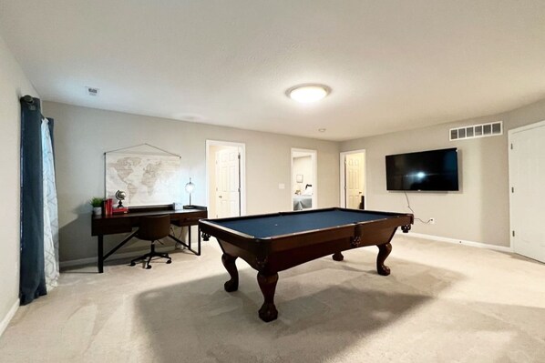 A room with a pool table, a desk with a chair, a map on the wall, and a TV mounted on the wall.