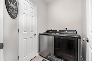 A laundry room with two stacked washers and dryers, a white door, and a wall-mounted sign.